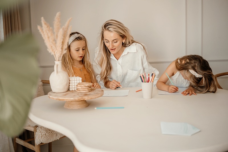 Family assistant tekent met twee meisjes aan de eettafel